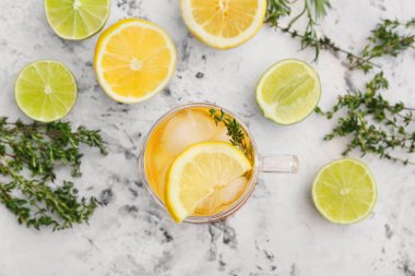 Bir fincan soğuk yeşil çay, bitki ve narenciye arkaplanda.