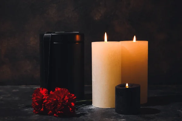 暗い背景にキャンドルやカーネーションの花と葬儀の骨壷 — ストック写真