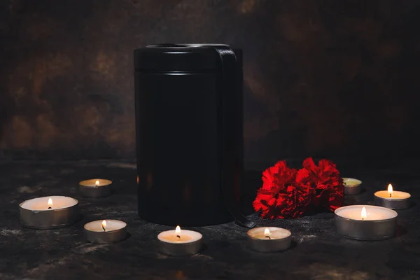 暗色の背景にカーネーションの花やキャンドルで葬儀の骨壷 — ストック写真
