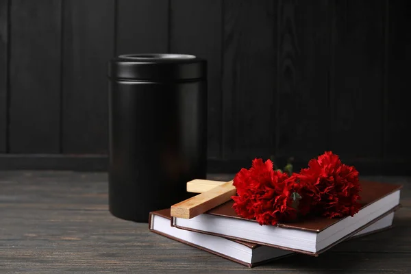 Carnation flowers with books and urn on dark wooden background