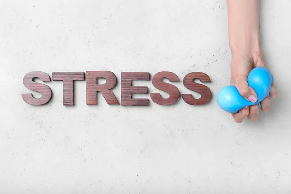 Female hand squeezing stress ball and word STRESS on light background