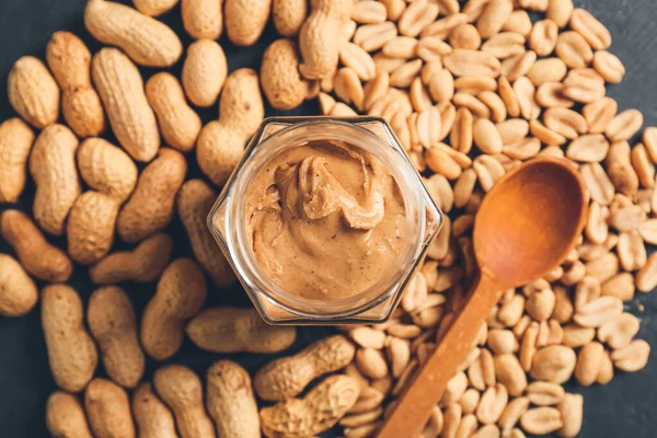 Jar with tasty peanut butter and nuts, closeup