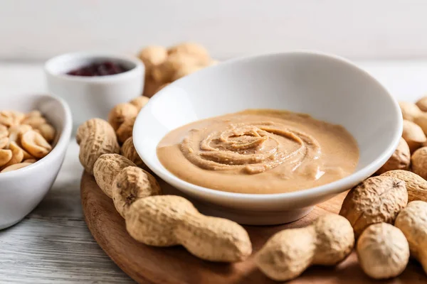Bowl with tasty peanut butter and nuts on light wooden background, closeup