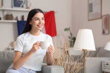 Genç Fransız kadın evdeki kanepede otururken çay içiyor.
