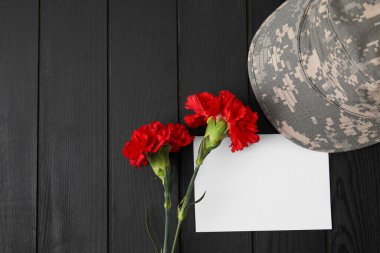 Askeri şapkalı karanfil çiçekleri ve koyu ahşap arka planda boş kağıt çarşaf.