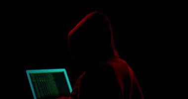 Karanlık arka planda dizüstü bilgisayarı olan bir hacker silueti