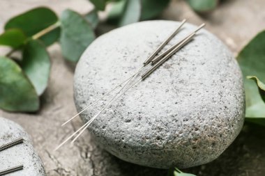 Gri arkaplanda akupunktur iğneleri ve spa taşı