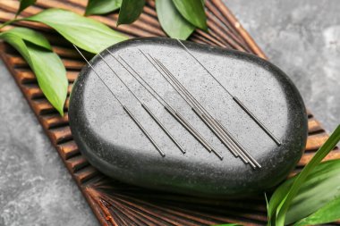 Gri arkaplanda akupunktur iğneleri ve spa taşı