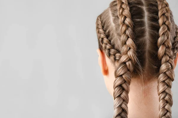 Beautiful young woman with braided hair on grey background