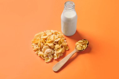 Lezzetli mısır gevrekli kaşık ve renkli arka planda bir şişe süt.