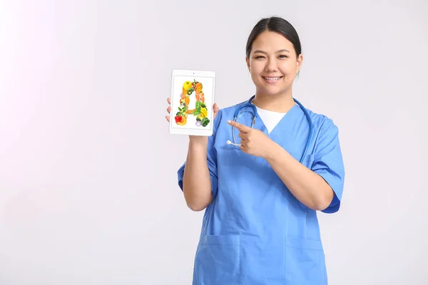 拥有富含维生素A的健康产品的亚洲医生 在平板电脑上进行轻度背景筛选 — 图库照片