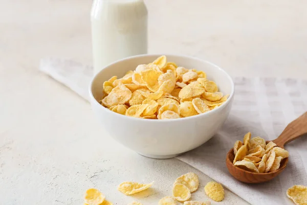 Bowl with tasty cornflakes and bottle of milk on light background