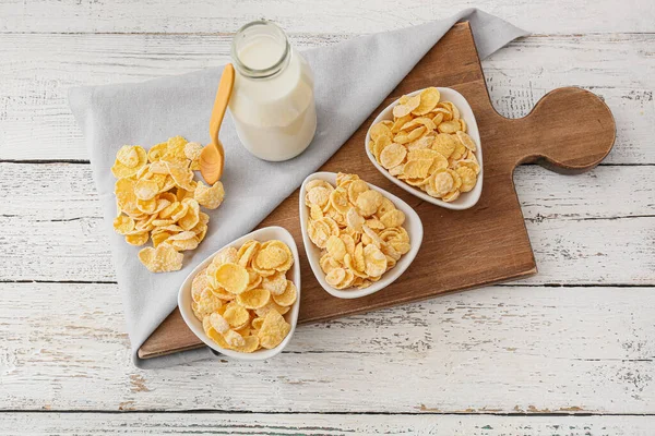 Bowls with tasty cornflakes and bottle of milk on light wooden background