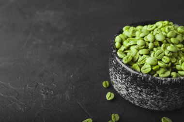 Koyu fonda yeşil kahve çekirdekleri olan bir kase.