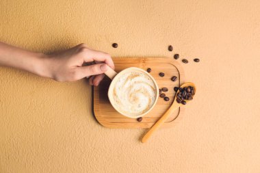 Arka planda bir fincan sıcak kapuçino ile kadın eli.