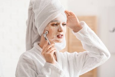 Yüzünde maske ve masaj aleti olan güzel bir kadın.