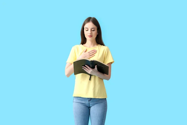 Young woman with Bible on color background