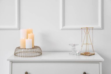 Aydınlık duvarın yanındaki çekmecelerin üzerinde yanan mumlar.