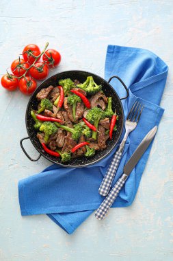 Frying pan with tasty beef and vegetables on light background clipart
