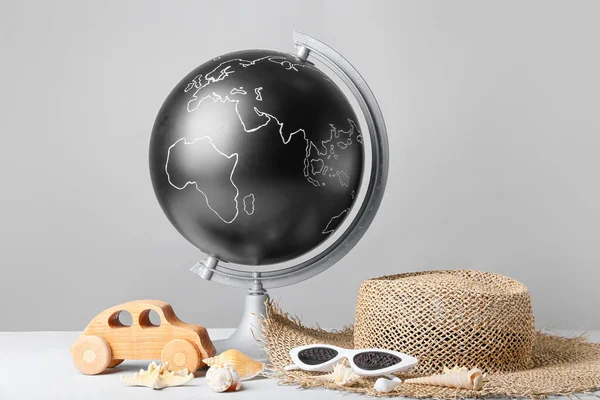 Globe with wooden car and beach accessories on grey background