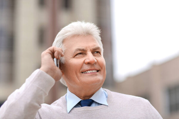 Старший бизнесмен разговаривает по мобильному телефону на улице