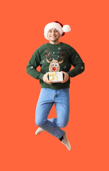 Jumping Junger Mann Weihnachtsmütze Mit Geschenkbox Auf Farbigem Hintergrund — Stockfoto