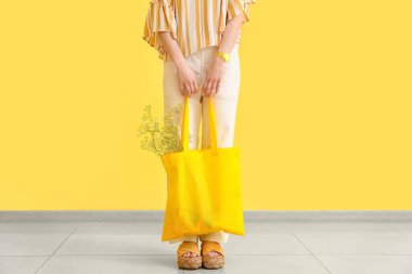Sarı duvarın yanında alışveriş çantalı şık genç bir kadın.