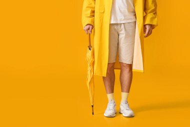 Sarı arka planda şemsiyesi olan şık bir genç.