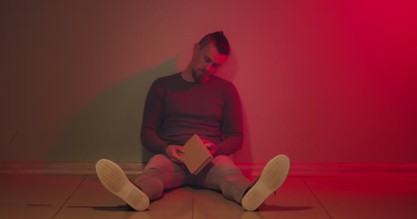 Депресивний Молодий Чоловік Книгою Сидить Підлозі Кімнаті — стокове відео