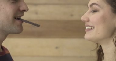 Mutlu genç çift, tahta arka planda çikolata yiyor.