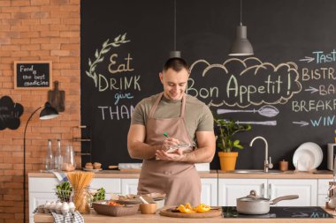 Mutfakta yemek tarifi kitabı olan genç bir adam.
