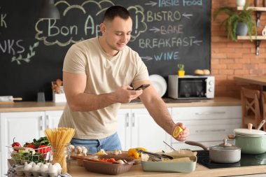 Genç adam mutfakta sebzeli fırında balık fotoğrafı çekiyor.