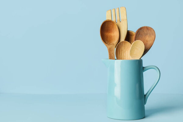 Wooden spoons and fork on color background