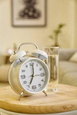 Çalar saat ve bir bardak su modern odadaki masada.