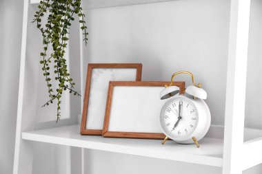Alarm saati ve beyaz duvarın yanındaki rafta boş fotoğraf çerçeveleri