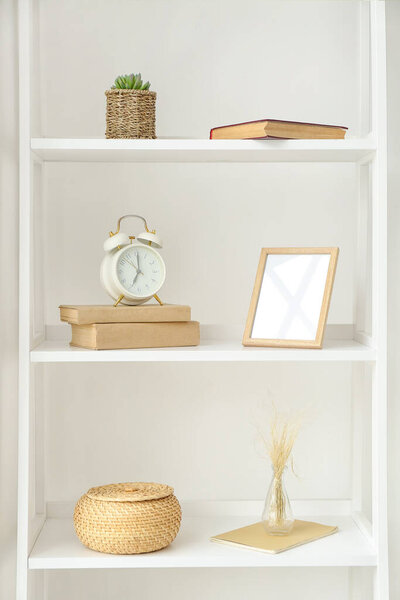 Shelves with alarm clock and decor near white wall