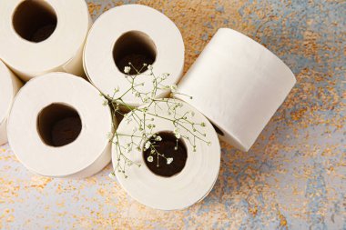 Tuvalet kağıdı ruloları ve arkaplanda çiçekler.