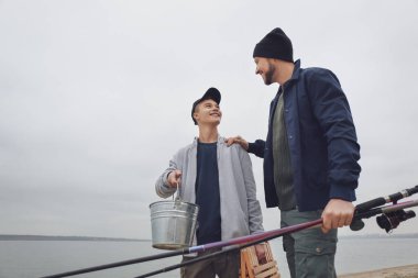Baba ve oğlu nehir kenarında balıkçılık ekipmanlarıyla