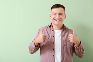 Sağlıklı dişleri olan genç bir adam arka planda baş parmak kaldırıyor.