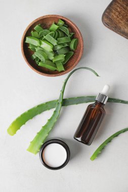 Bir şişe yağ, kremalı kavanoz ve arka planda aloe parçaları.