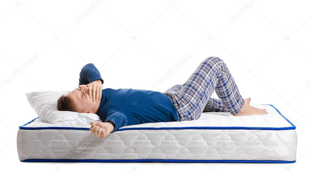 Young man lying on soft mattress against white background