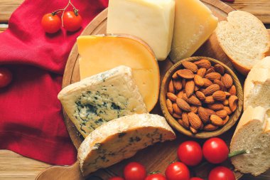 Tahta arka planda farklı peynir, domates, fındık ve ekmek türleri olan tahta, yakın plan.