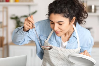 Genç kadın mutfakta yemek tadıyor.