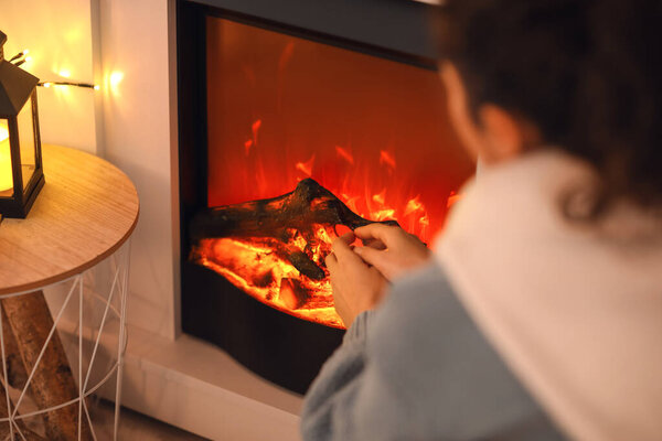 Young woman warming hands near fireplace at home