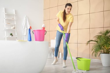 Banyoda yerleri paspaslayan genç bir kadın.