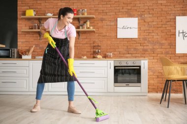 Mutfakta yerleri paspaslayan genç kadın.