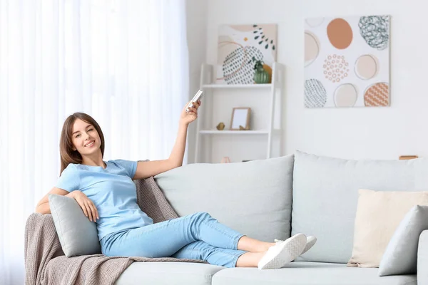 Young woman with air conditioner remote control at home