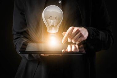 Tablet bilgisayarlı iş kadını ve arka planda parlayan ampul, yakın plan.