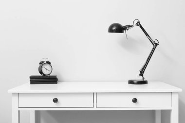 Table with lamp and alarm clock near light wall