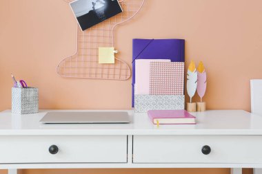 Modern laptop and organizers on table near color wall